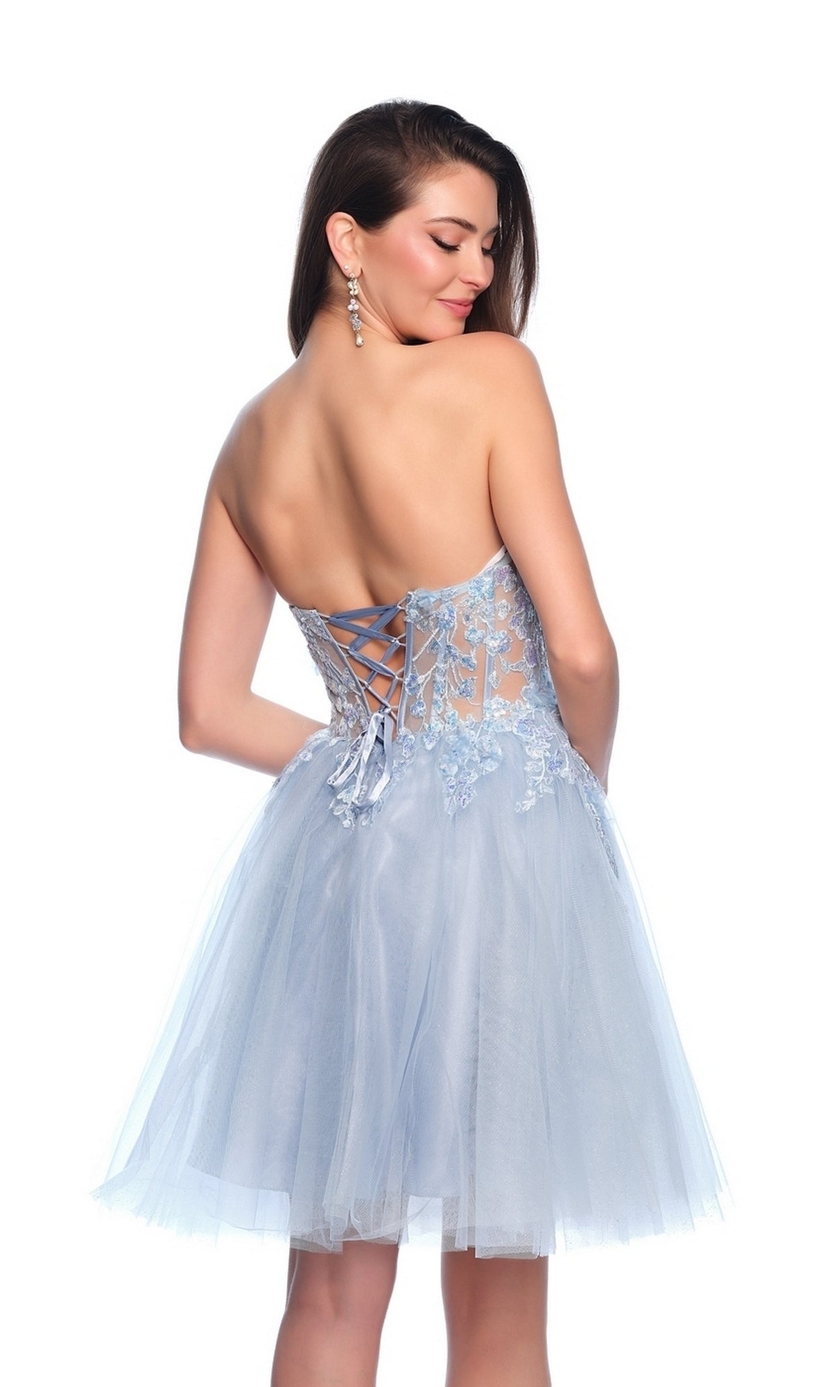 Woman wearing the Sheer Glitter Homecoming Dress 11973, featuring light blue floral embroidery, a lace-up back, and a tulle skirt, faces away while looking over her shoulder.